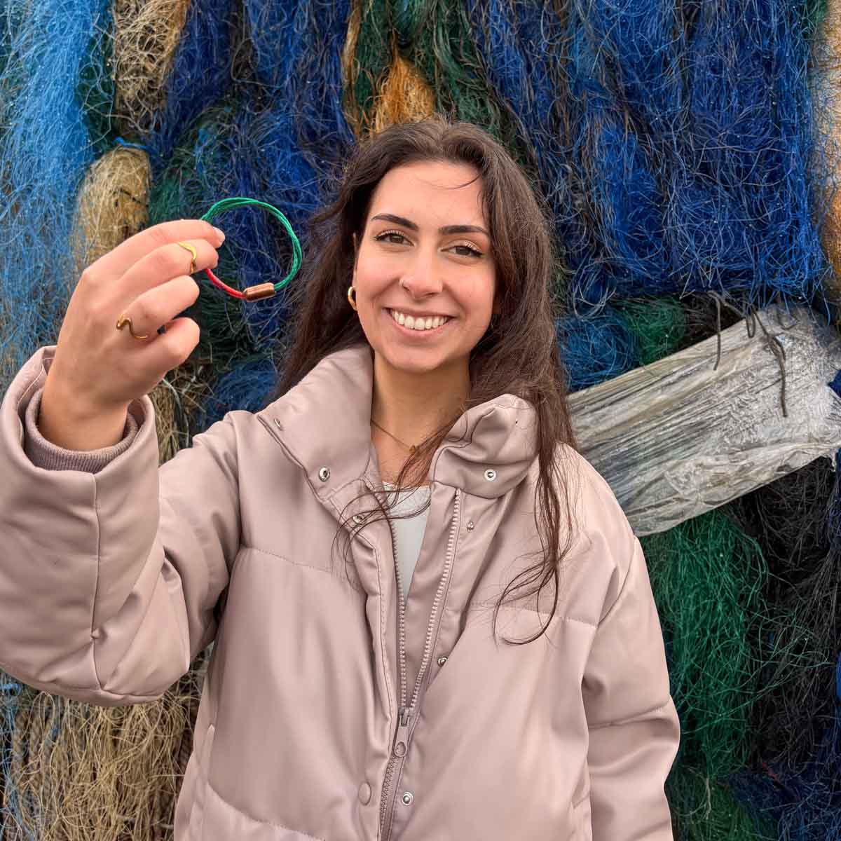 Person hält das BRACENET Christmas Bracenet aus einem grünen und einem roten Fischernetz mit coffee Magnetverschluss vor sich und lacht. 