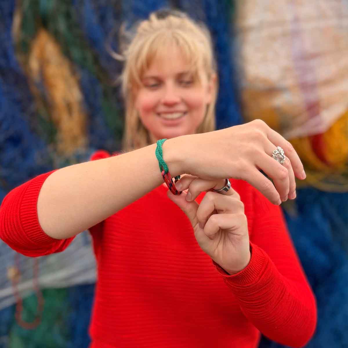 Person trägt das BRACENET Christmas Bracenet aus einem grünen und einem roten Fischernetz mit coffee Magnetverschluss am Handgelenk und schaut es lachend an.