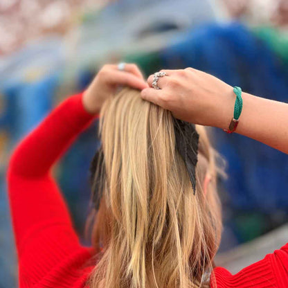 Person trägt das BRACENET Christmas Bracenet aus einem grünen und einem roten Fischernetz mit coffee Magnetverschluss m Handgelenk und macht sich einen Zopf.