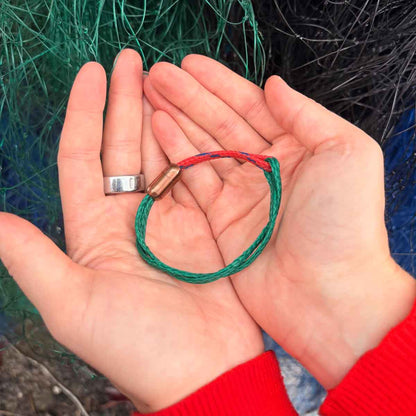 Person hält BRACENET Christmas Bracenet aus einem grünen und einem roten Fischernetz mit coffee Magnetverschluss in den Händen über Fischernetzen.