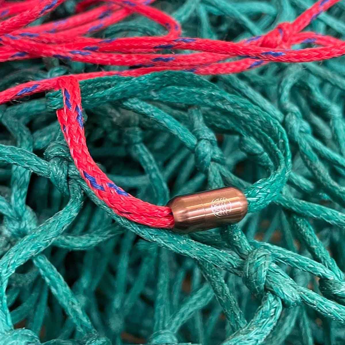Das BRACENET Christmas Bracenet aus einem grünen und einem roten Fischernetz mit coffee Magnetverschluss liegt auf den Fischernetzen.