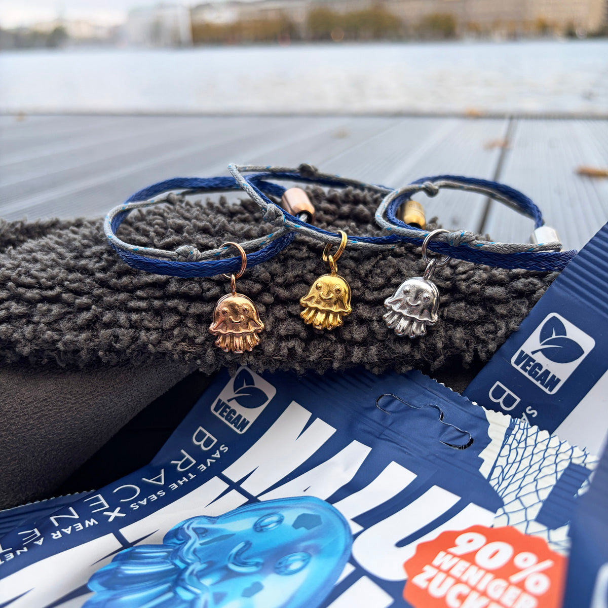 3 Nalu Bracenet Armbänder mit Quallen Anhänger in den Farben rosé, gold und ilber und im Vordergrund eine Nalu Tüte