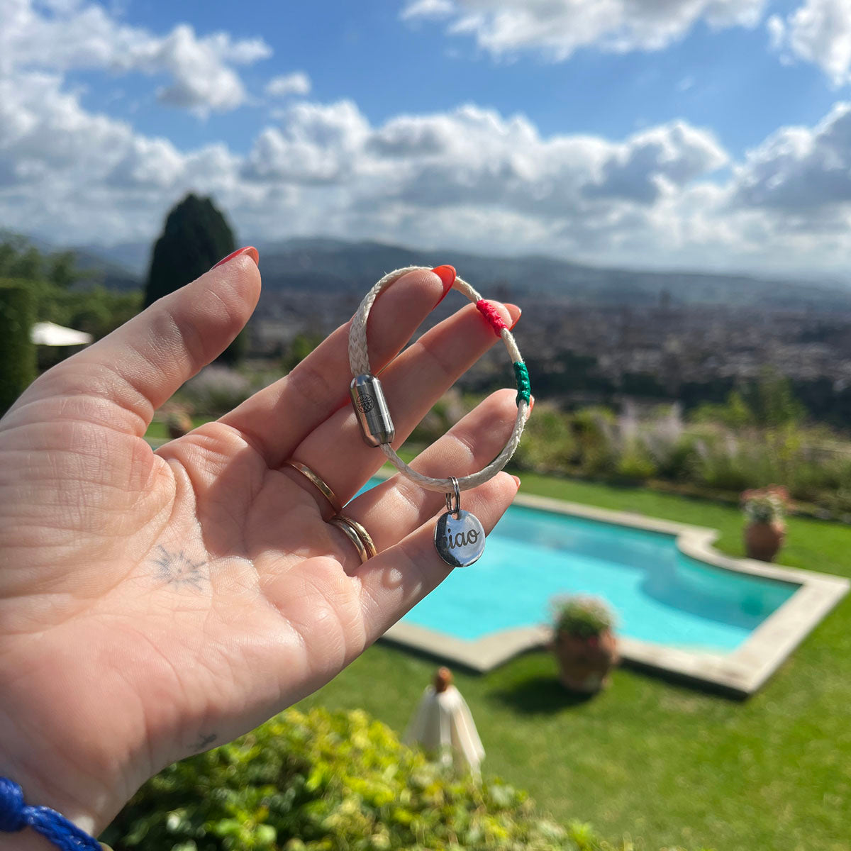Italy, Italien Bracenet Bracelet  aus ehemaligem Fischernetz in Weiß mit roten und grünen Akzenten mit Edelstahl Magnetverschluss und einem Edelstahlanhänger mit Ciao Gravur in der Hand gehalten