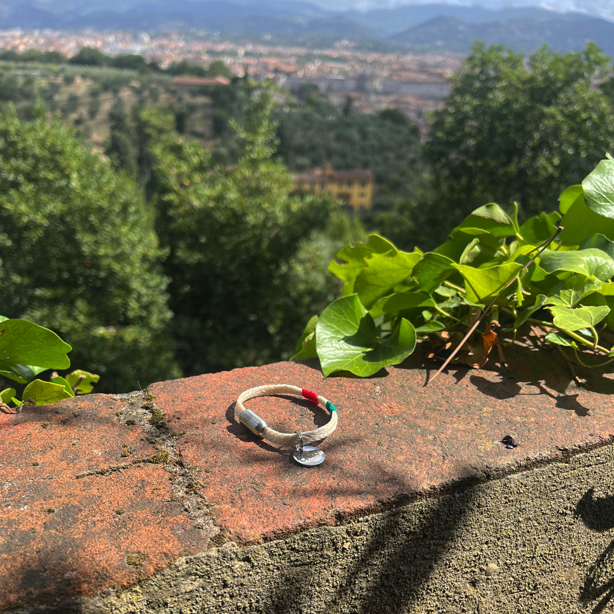 Italy, Italien Bracenet Bracelet  aus ehemaligem Fischernetz in Weiß mit roten und grünen Akzenten mit Edelstahl Magnetverschluss und einem Edelstahlanhänger mit Ciao Gravur liegend auf einer Mauer