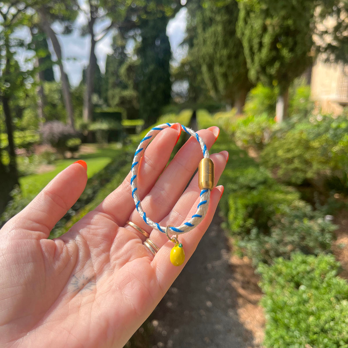Almalfi Bracenet Bracelet aus Fischernetz in weiß und blau mit Edelstahl Magnetverschluss und einem Zitronenanhänger in der Hand