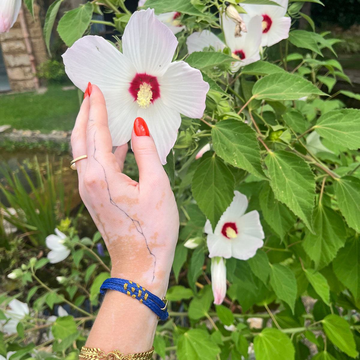 Sicilia, Sizilien Bracenet Bracelet aus Fischernetz in blau und gold mit Edelstahl Magnetverschluss und einem Medusa Anhänger am Handgelenk mit Blume in der Hand