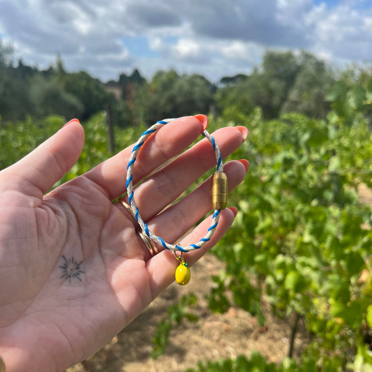 Almalfi Bracenet Bracelet aus Fischernetz in weiß und blau mit Edelstahl Magnetverschluss und einem Zitronenanhänger in der Hand 