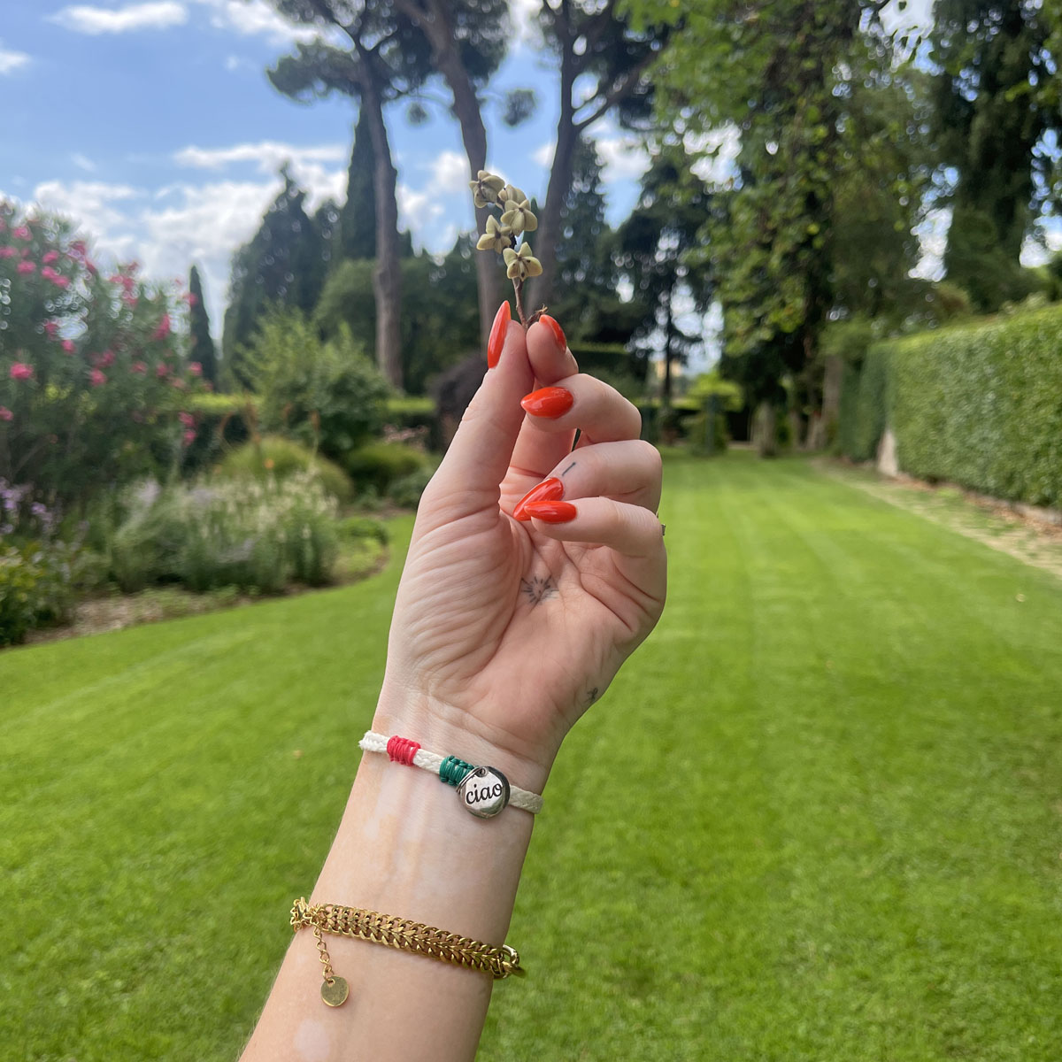 Italy, Italien Bracenet Bracelet  aus ehemaligem Fischernetz in Weiß mit roten und grünen Akzenten mit Edelstahl Magnetverschluss und einem Edelstahlanhänger mit Ciao Gravur am Handgelenk mit Blume in der Hand