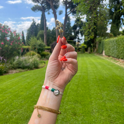 Italy, Italien Bracenet Bracelet  aus ehemaligem Fischernetz in Weiß mit roten und grünen Akzenten mit Edelstahl Magnetverschluss und einem Edelstahlanhänger mit Ciao Gravur am Handgelenk mit Blume in der Hand