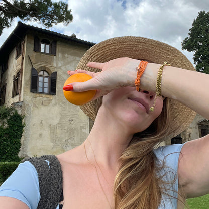 La Dolce Vita Toskana Bracenet Bracelet aus Fischernetz in orange mit Edelstahl Magnetverschluss und einem Edelstahlanhänger mit La Dolce Vita Gravur am Handgelenk mit Orange in der Hand von Madeleine