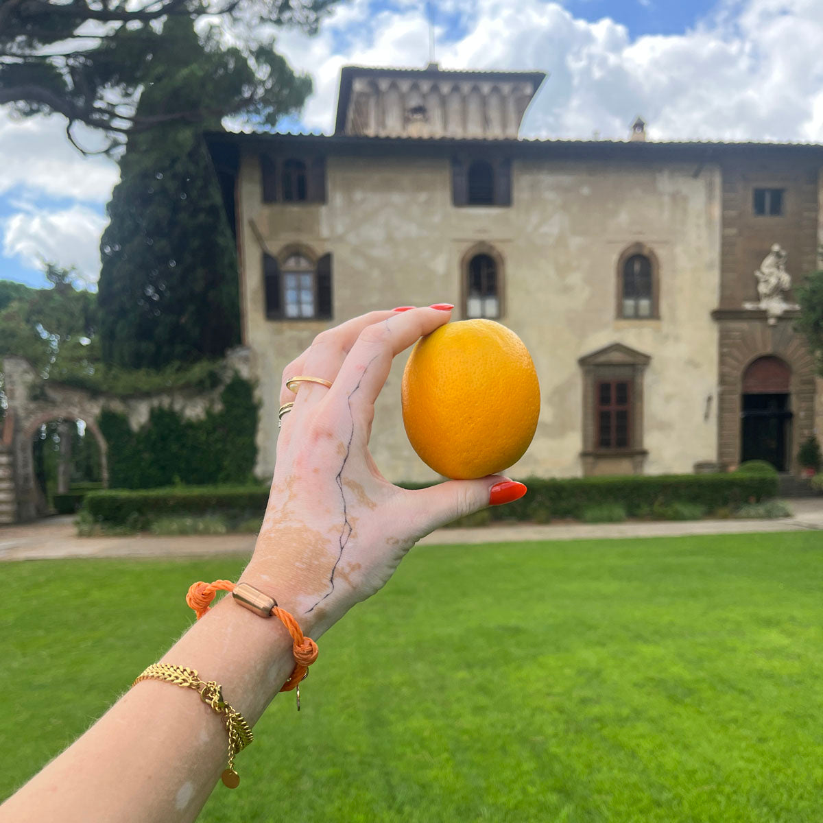 La Dolce Vita Toskana Bracenet Bracelet aus Fischernetz in orange mit Edelstahl Magnetverschluss und einem Edelstahlanhänger mit La Dolce Vita Gravur am Handgelenk und Orange in der Hand