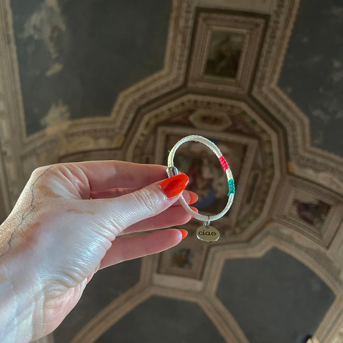 Italy, Italien Bracenet Bracelet  aus ehemaligem Fischernetz in Weiß mit roten und grünen Akzenten mit Edelstahl Magnetverschluss und einem Edelstahlanhänger mit Ciao Gravur in der Hand gehalten