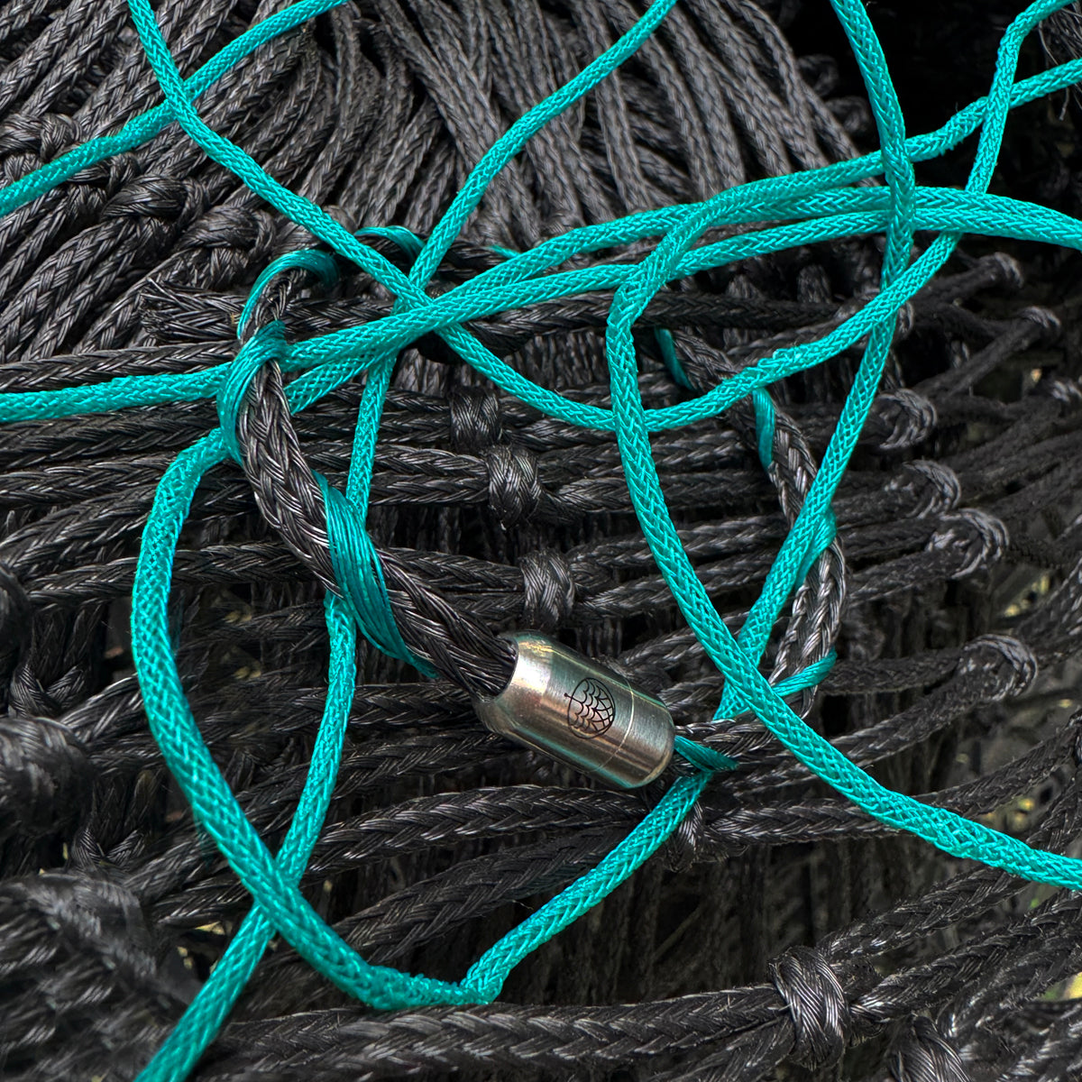 November BRACENET Upcycling Armband Timor Sea aus schwarzen und petrolfarbenen Fischernetzen mit silber Verschluss liegt auf Fischernetzen. 