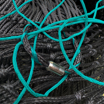 November BRACENET Upcycling Armband Timor Sea aus schwarzen und petrolfarbenen Fischernetzen mit silber Verschluss liegt auf Fischernetzen. 