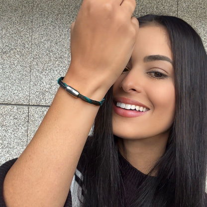 Person trägt das November BRACENET Upcycling Armband Timor Sea aus schwarzen und petrolfarbenen Fischernetzen mit silber Verschluss am Handgelenk, hält den Arm hoch und lächelt.