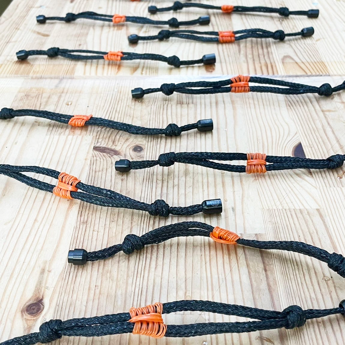 Die fertigen BRACENET Upcycling Armband Pumpkin Bay II aus schwarzen alten Fischernetzen mit einem Knoten aus orangenen Dolly Ropes und einem schwarzen Magnetverschluss liegen auf dem tisch in der Produktion. 