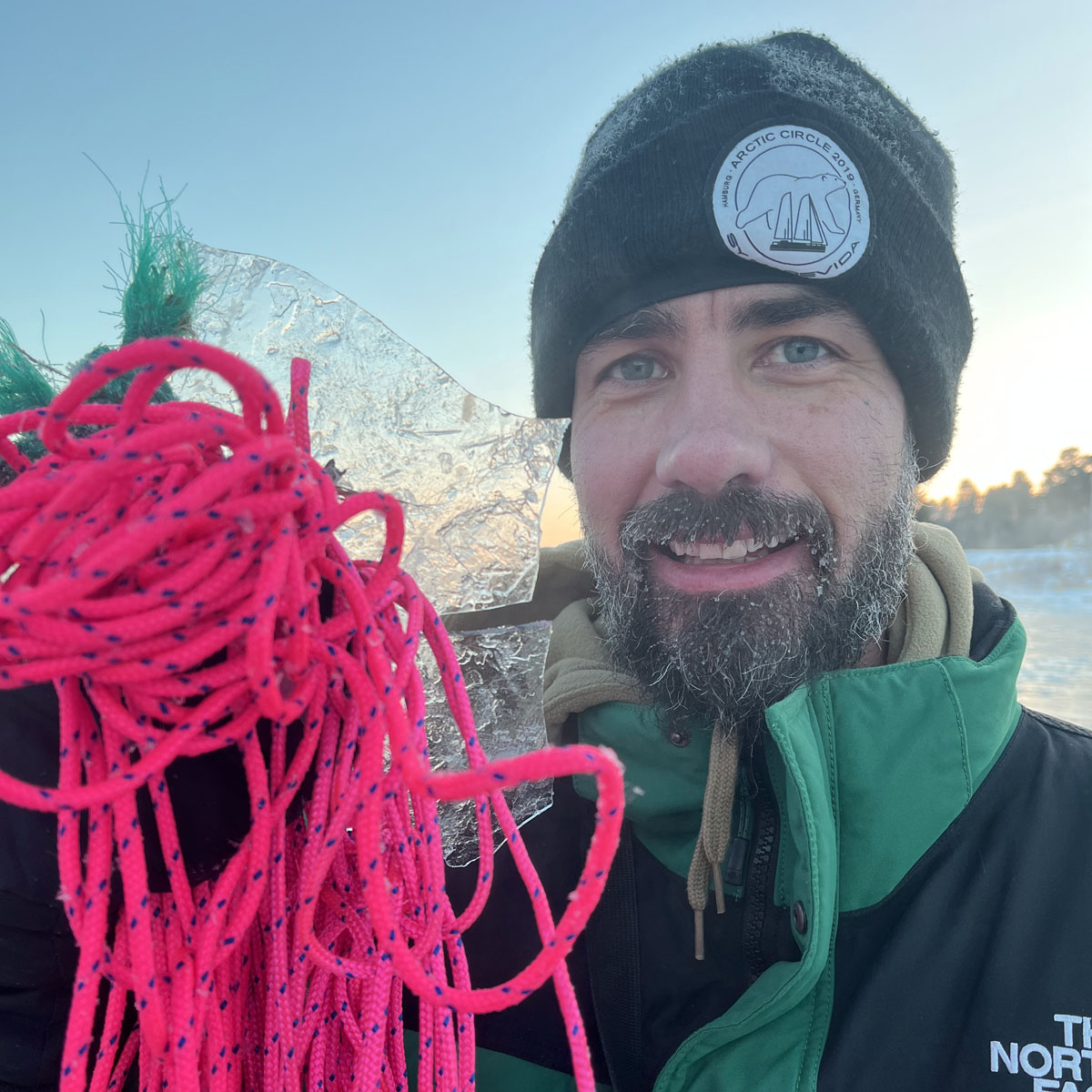 Person hält das Gulf of Bothnia Fischernetz in Pink in der Hand neben das Gesicht. 