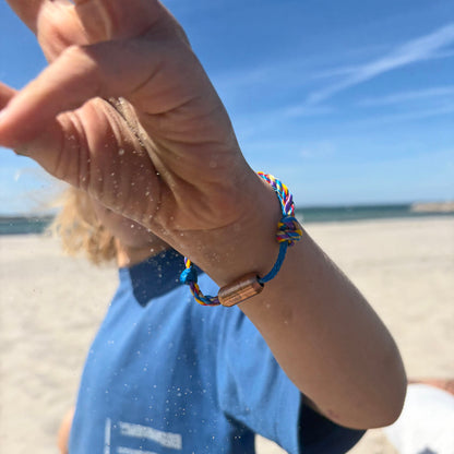 Kind ist am Strand und trägt das Kids' Bracenet Lübecker Bucht aus einem Strang blauem Fischernetz und einem Strang buntem Fischernetz, größenverstellbar mit Magnetverschluss in Roségold.  