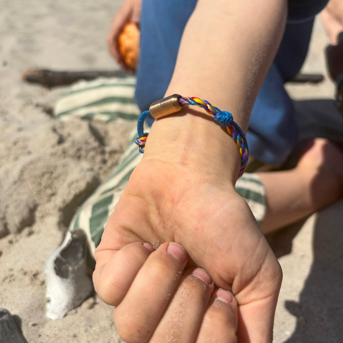 Kind trägt das Kids' Bracenet Lübecker Bucht aus einem Strang blauem Fischernetz und einem Strang buntem Fischernetz, größenverstellbar mit Magnetverschluss in Roségold.  