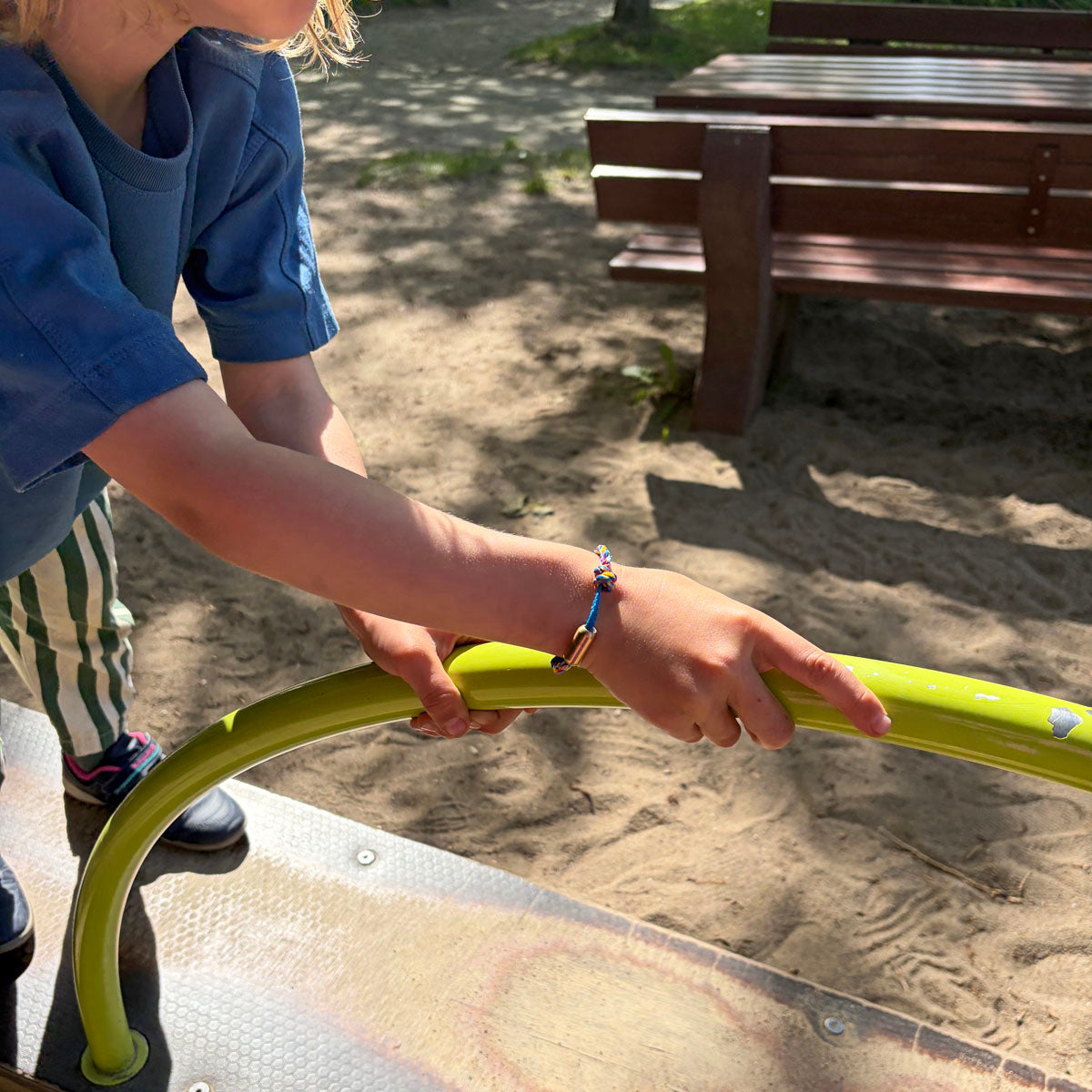 Kind trägt das Kids' Bracenet Lübecker Bucht aus einem Strang blauem Fischernetz und einem Strang buntem Fischernetz, größenverstellbar mit Magnetverschluss in Roségold und hält sich an einer Stange fest. 