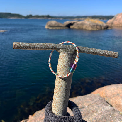 Das BRACENET Upcycling Armband Rainbow Bay aus alten weißen Fischernetzen mit bunten Dolly Ropes umwickelt und bunten Magnetverschluss mit Farbverlauf hängt am Steg, im Hintergrund ein Fjord