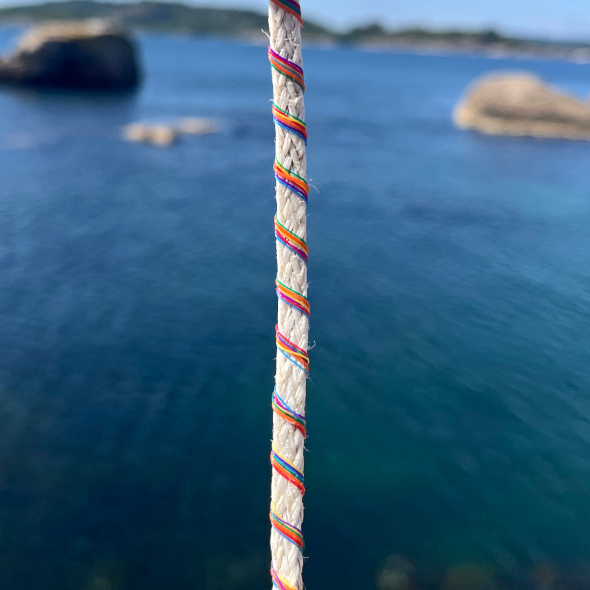 Nahansicht des BRACENET Upcycling Armband Rainbow Bay aus alten weißen Fischernetzen mit bunten Dolly Ropes umwickelt, im Hintergrund das Meer