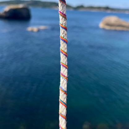 Nahansicht des BRACENET Upcycling Armband Rainbow Bay aus alten weißen Fischernetzen mit bunten Dolly Ropes umwickelt, im Hintergrund das Meer