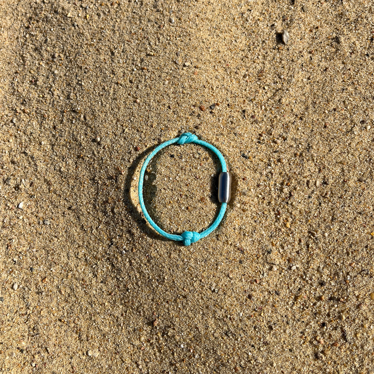 Das BRACENET Upcycling Armband Glacier Bay aus eisblauen Fischernetzen mit 2 Knoten und silbernen Bajonettverschluss liegt im Sand