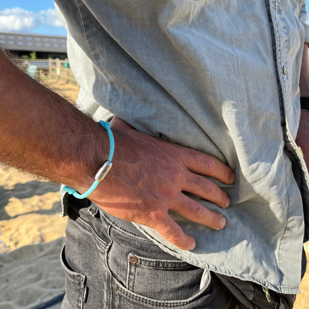 Person trägt das BRACENET Upcycling Armband Glacier Bay aus eisblauen Fischernetzen und 2 Knoten mit silbernen Bajonettverschluss am Handgelenk, im Hintergrund Sand