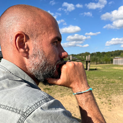 Person trägt das BRACENET Upcycling Armband Glacier Bay aus eisblauen Fischernetzen mit 2 Knoten und silbernen Bajonettverschluss am Handgelenk, im Hintergrund ein Spielplatz