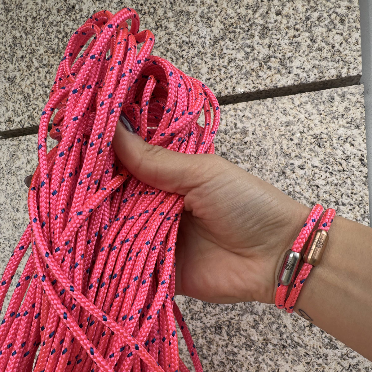 Person trägt zwei Gulf of Bothnia Bracenets aus Fischernetz in Pink mit blauen Punkten und Magnetverschluss in Roségold oder Silber am Handgelenk und hält das Fischernetz in der Hand. 