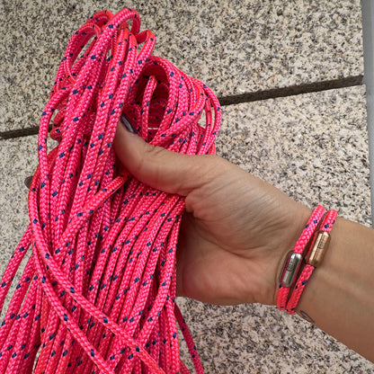 Person trägt zwei Gulf of Bothnia Bracenets aus Fischernetz in Pink mit blauen Punkten und Magnetverschluss in Roségold oder Silber am Handgelenk und hält das Fischernetz in der Hand. 