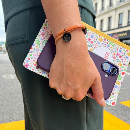 Person trägt das BRACENET Upcycling Armband Ghost Diving USA aus orangenen alten Fischernetzen und einem schwarzen Magnetverschluss und Edelstahlanhänger am Handgelenk und geht mit einem Notizheft und Mobiltelefon über die Straße