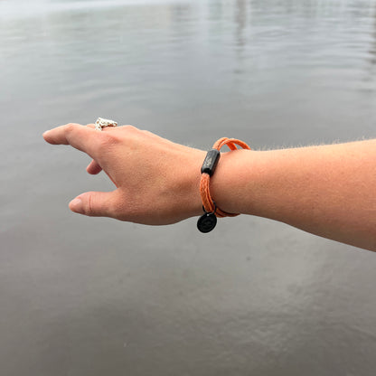 Person trägt das BRACENET Upcycling Armband Ghost Diving USA aus orangenen alten FIschernetzen und einem schwarzen Magnetverschluss und Edelstahlanhänger am Handgelenk, im Hintergrund die Alster
