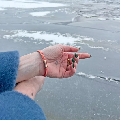 Person trägt Februar Bracenet Amur Bay aus lachsfarbenen Fischernetz mit roten Dolly Ropes verziert und mit roségoldenen Magnetverschluss am Handgelenk und zeigt aufs Wasser. 
