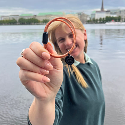 Person zeigt das BRACENET Upcycling Armband Ghost Diving USA aus orangenen alten FIschernetzen und einem schwarzen Magnetverschluss und Edelstahlanhänger, im Hintergrund die Alster