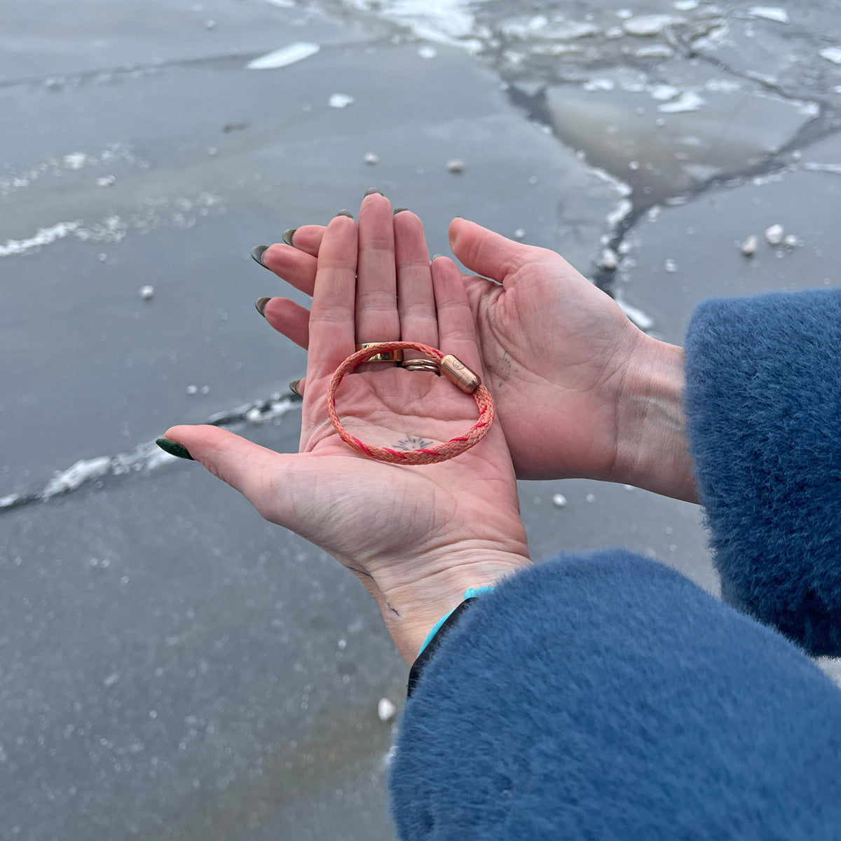 Person hält das Februar Bracenet Amur Bay aus lachsfarbenen Fischernetz mit roten Dolly Ropes verziert und mit roségoldenen Magnetverschluss in beiden Händen über dem Wasser. 