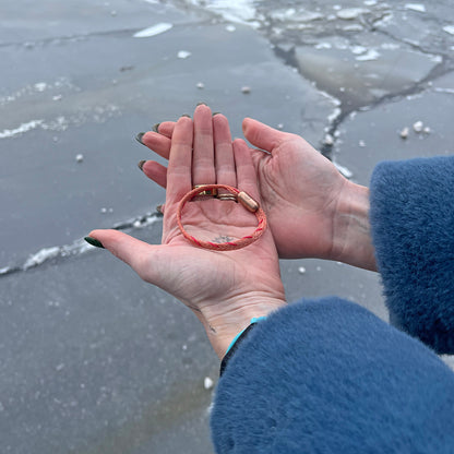 Person hält das Februar Bracenet Amur Bay aus lachsfarbenen Fischernetz mit roten Dolly Ropes verziert und mit roségoldenen Magnetverschluss in beiden Händen über dem Wasser. 