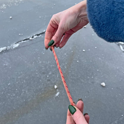 Person hält das Februar Bracenet Amur Bay aus lachsfarbenen Fischernetz mit roten Dolly Ropes verziert und mit roségoldenen Magnetverschluss gestreckt, so dass man die Verzierungen sieht. 