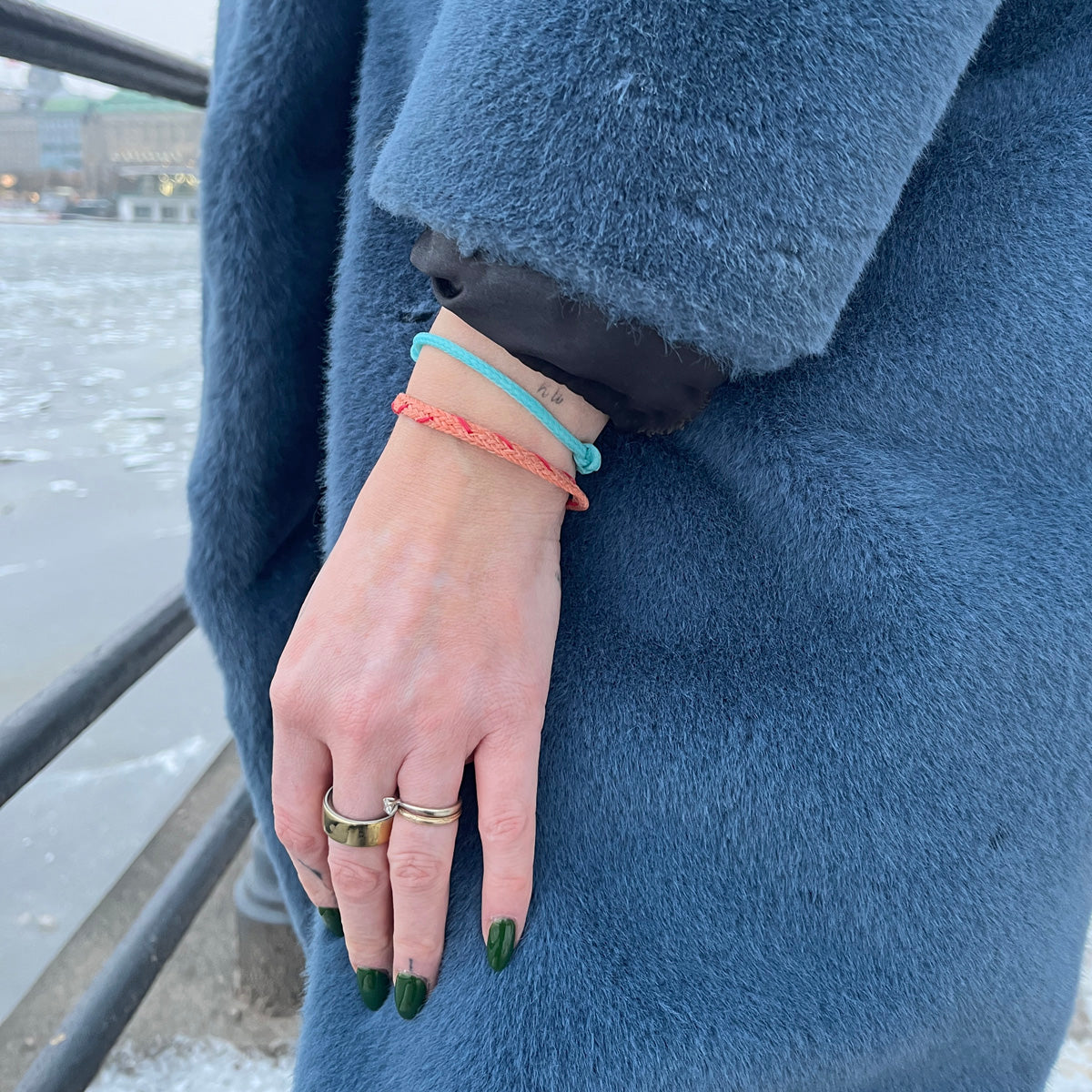 Person trägt das Februar Bracenet Amur Bay aus lachsfarbenen Fischernetz mit roten Dolly Ropes verziert und mit roségoldenen Magnetverschluss am Handgelenk und lässt die Hand hängen. 