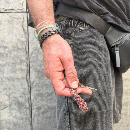 Person hält den BRACENET Schlüsselanhänger Gulf of California aus bunten Fischereiseilen mit Makramee und mit roségoldenem Schlüsselanhänger-Ring und Anhänger mit Delfin Gravurin der Hand. 