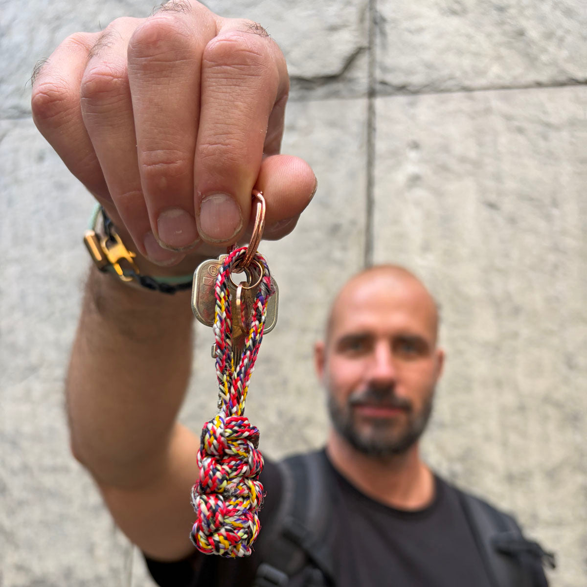 Person hält BRACENET Schlüsselanhänger Gulf of California aus bunten Fischereiseilen mit Makramee und mit roségoldenem Schlüsselanhänger-Ring und Anhänger mit Delfin Gravur vor sich 