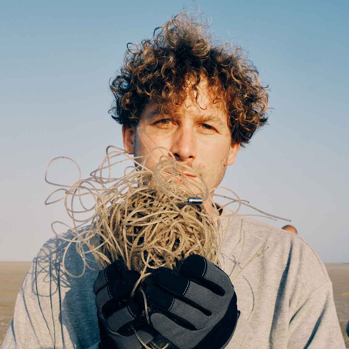 Malte Zierden steht am Strand und hält die transparenten Langleinen in der Hand auf denen das Alles für die Tiere immer - Robbe "Walvis" Armband aus transparenten Langleinen von BRACENET mit Drehverschluss in silber und "Alles für die Tiere, immer" Gravur mit Robben-Motiv liegt.