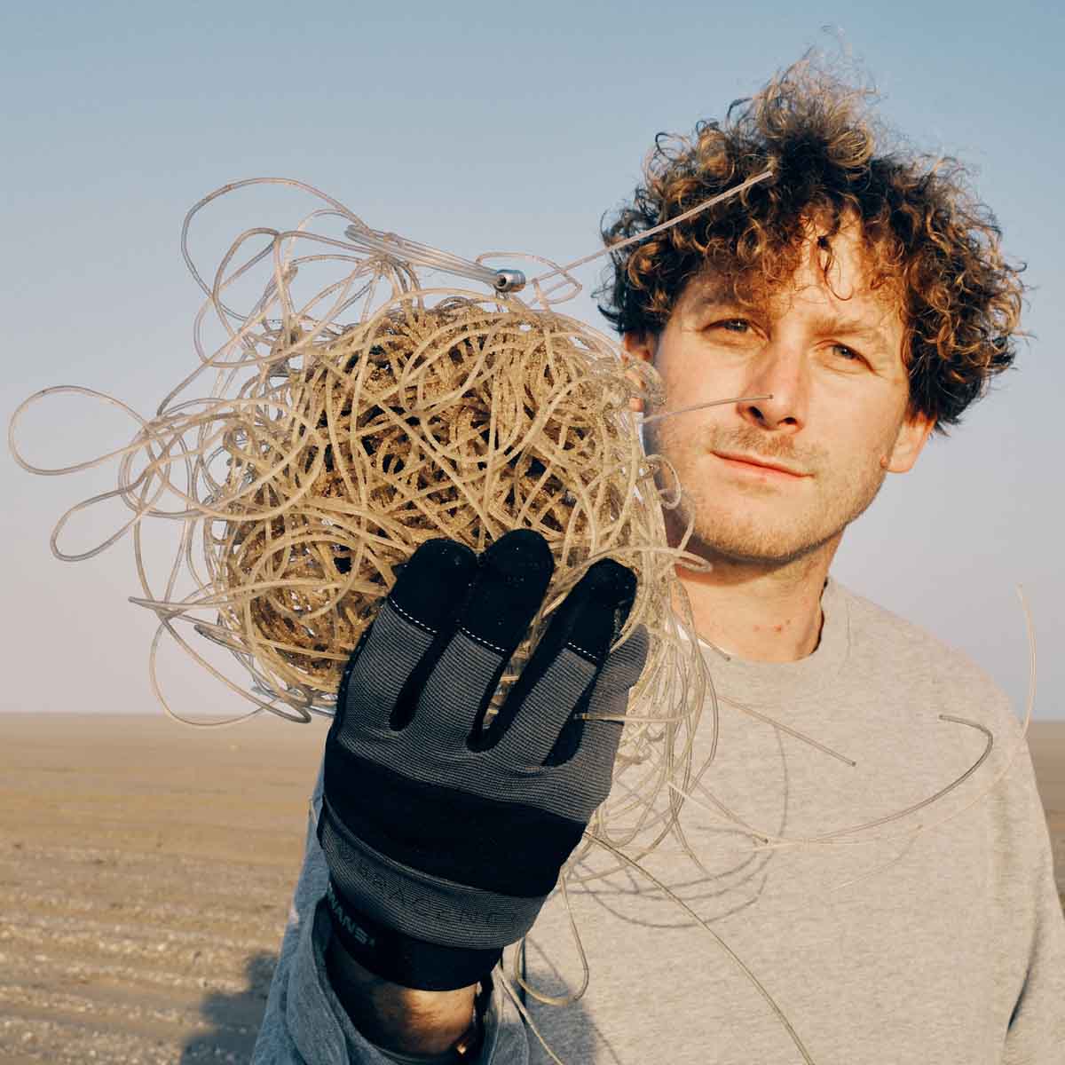 Malte Zierden steht am Strand und hält die transparenten Langleinen in der Hand auf denen das Alles für die Tiere immer - Robbe "Walvis" Armband aus transparenten Langleinen von BRACENET mit Drehverschluss in silber und "Alles für die Tiere, immer" Gravur mit Robben-Motiv liegt.