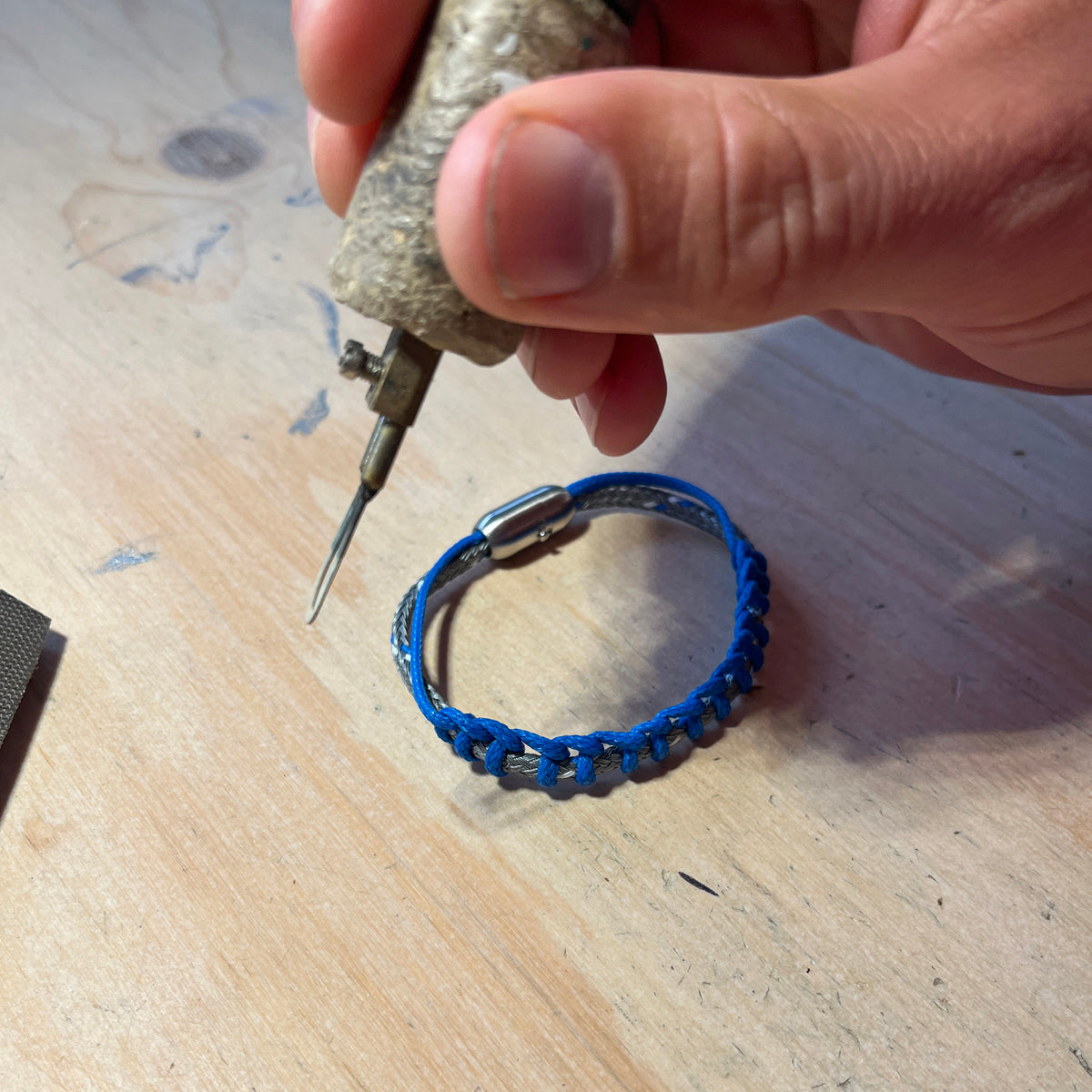 BRACENET Upcycling Armband Scotia Sea aus grauen und blauen alten Fischernetzen und einem silbernen Bajonettverschluss wir gefertig. Man sieht den Lötkolben im Bild.