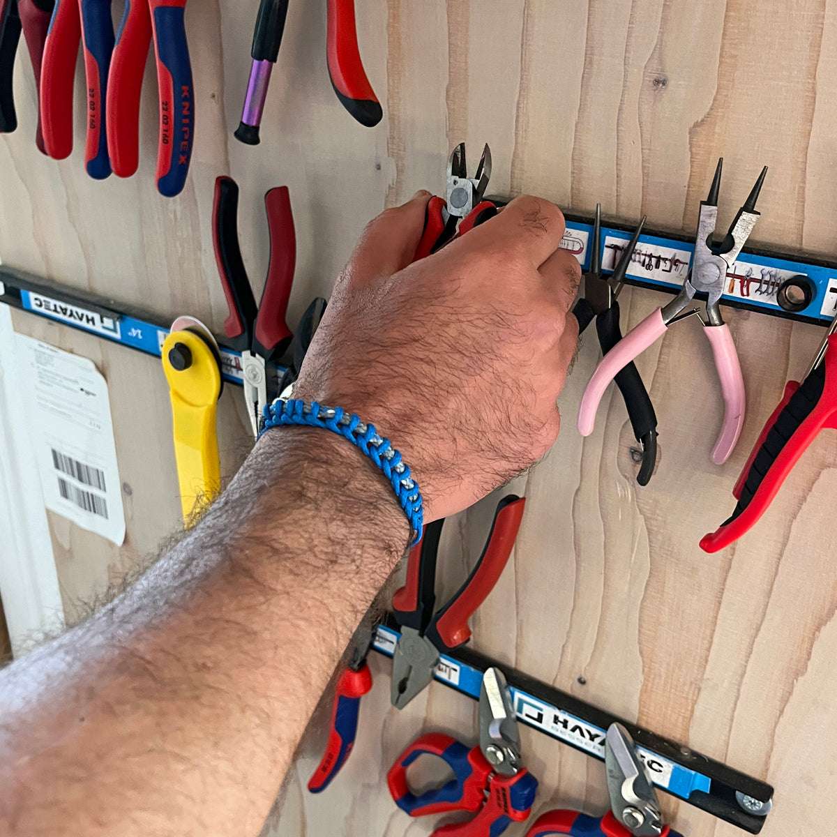 Person trägt das BRACENET Upcycling Armband Scotia Sea aus grauen und blauen alten Fischernetzen am Handgelenk und greift nach Werkzeug zum fertigen. 