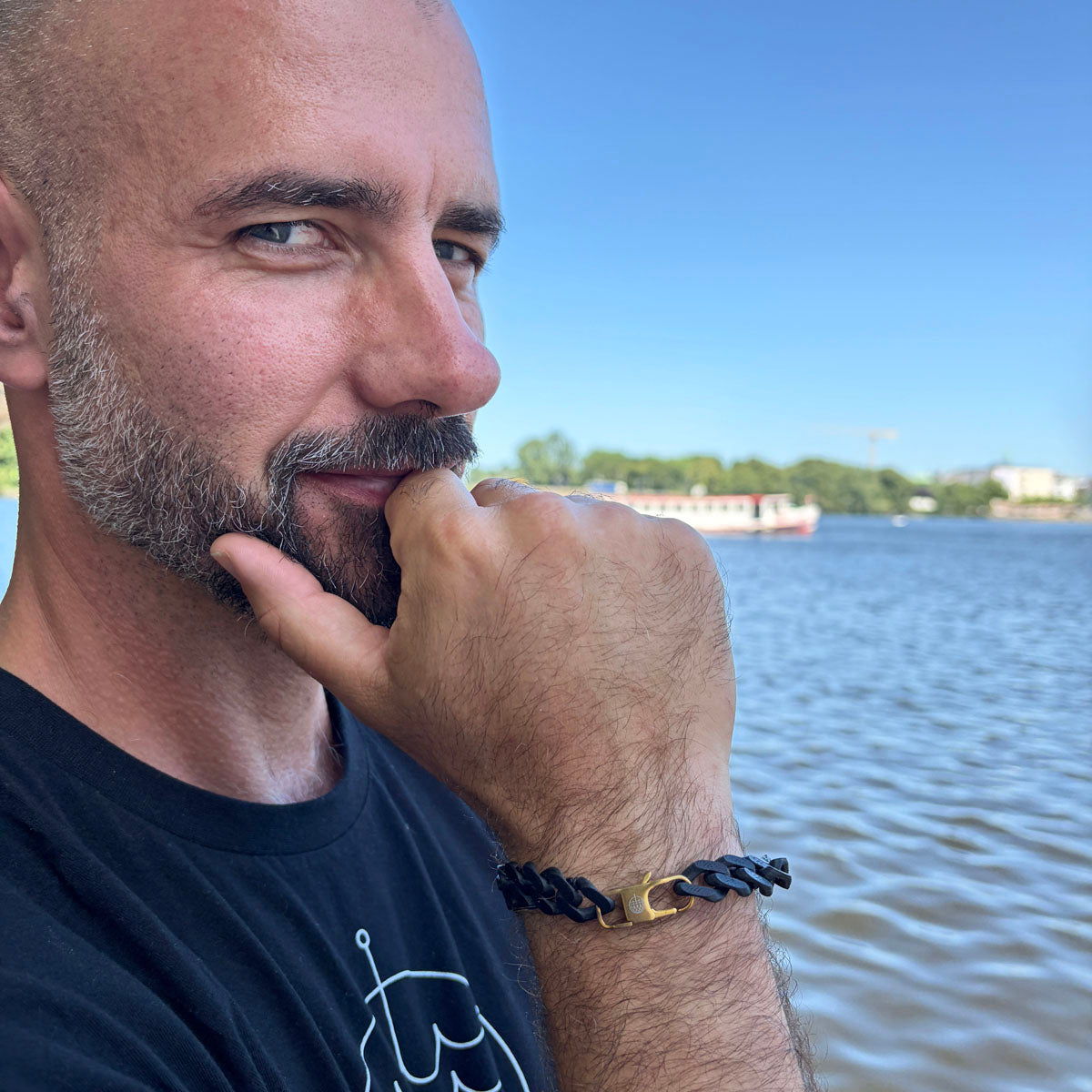 Person trägt das SeaChain Bracenet in 3D Druck aus alten Fischernetzen hergestellt in Schwarz mit kleinem Clip Karabiner in Gold am Handgelenk und hat die Hand am Kinn.