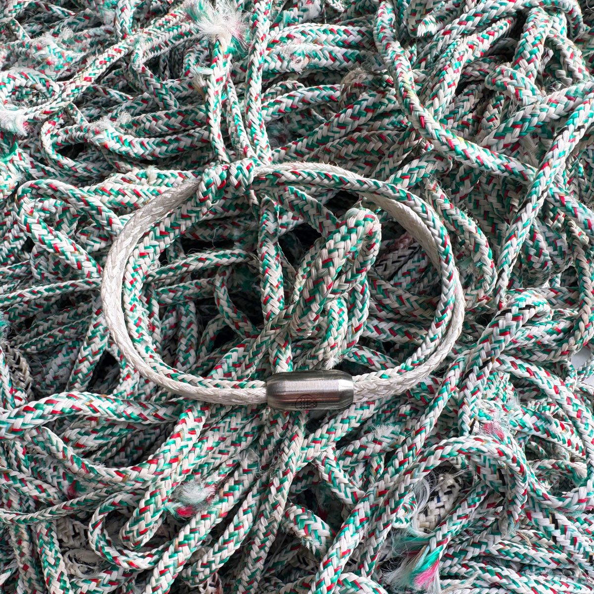 Das Enard Bay Bracenet aus Fischernetz in Weiß und Grün mit Umwicklung in der Mitte und mit Bajonettverschluss in Silber liegt auf Fischernetzen. 