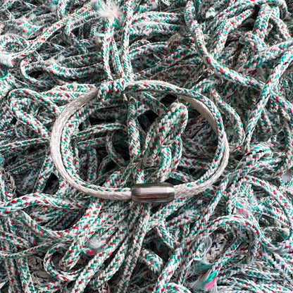 Das Enard Bay Bracenet aus Fischernetz in Weiß und Grün mit Umwicklung in der Mitte und mit Bajonettverschluss in Silber liegt auf Fischernetzen. 