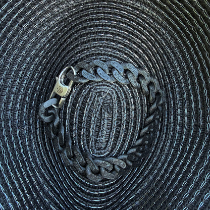 Das SeaChain Bracenet in 3D Druck aus alten Fischernetzen hergestellt in Schwarz mit kleinem Clip Karabiner in Silber liegt auf einem Sonnenhut.